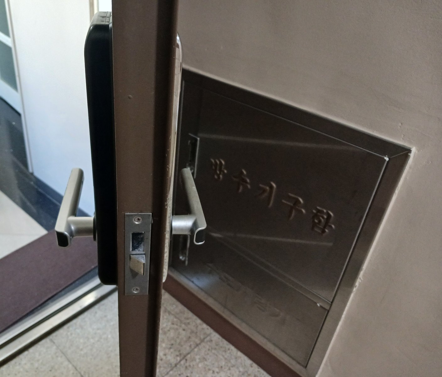 서울시 광진구 출장 — 열어 둔 갈색 철문 옆면의 걸쇠와 양쪽 은색 레버, 뒤쪽 벽에 묻힌 금속 함